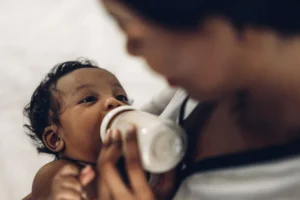 baby with dark skin being held by adult while being fed a bottle